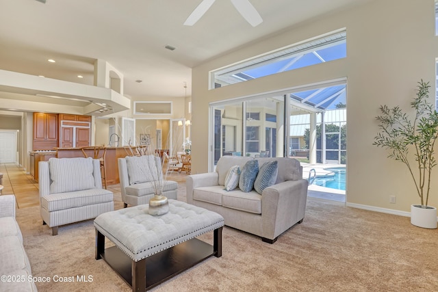 living area with a towering ceiling, a ceiling fan, light colored carpet, and baseboards