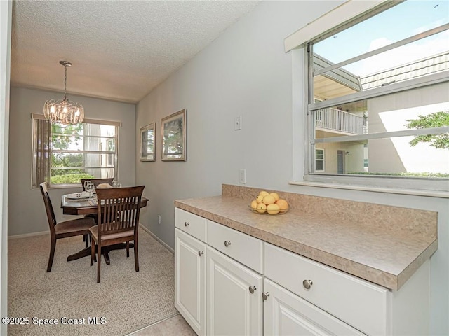 dining room with a textured ceiling, a chandelier, baseboards, and light colored carpet