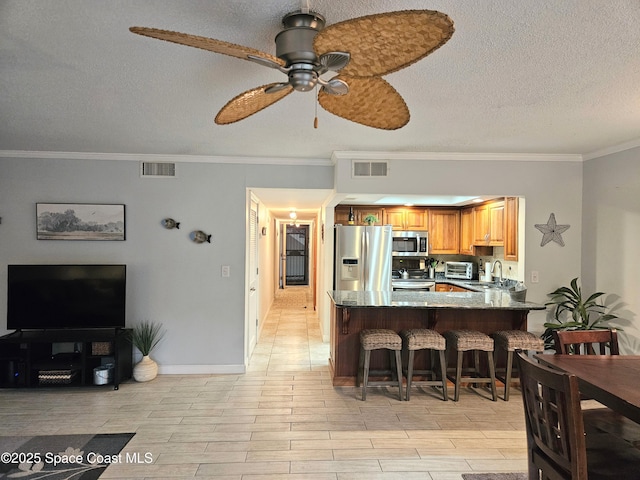 1700 S Atlantic Ave Unit 107, Cocoa Beach, FL 32931 - kitchen featuring appliances with stainless steel finishes, a peninsula, a ceiling fan, a textured ceiling, and crown molding