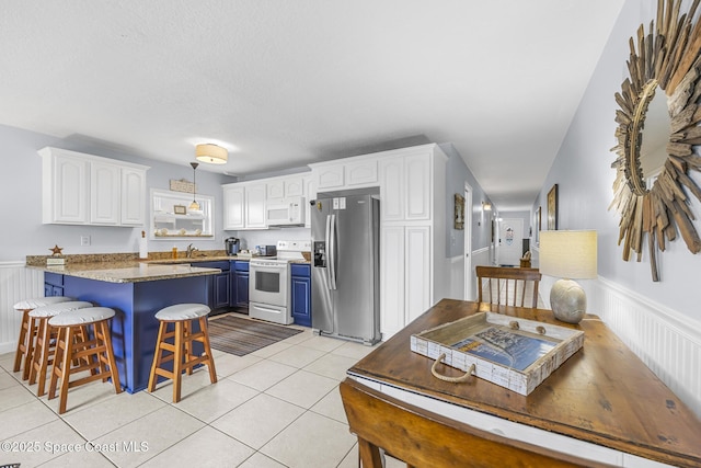 1145 S Atlantic Ave Unit B, Cocoa Beach, FL 32931 - kitchen featuring white appliances, blue cabinets, white cabinets, a breakfast bar area, and a peninsula