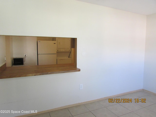 unfurnished room featuring stacked washer / drying machine, tile patterned flooring, and baseboards