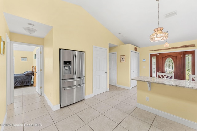 kitchen featuring stainless steel fridge, lofted ceiling, light tile patterned floors, light stone counters, and baseboards