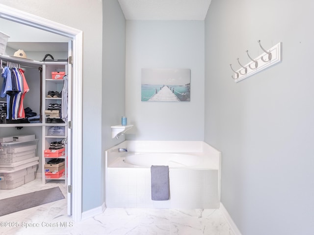 full bathroom featuring marble finish flooring, a walk in closet, a garden tub, and baseboards