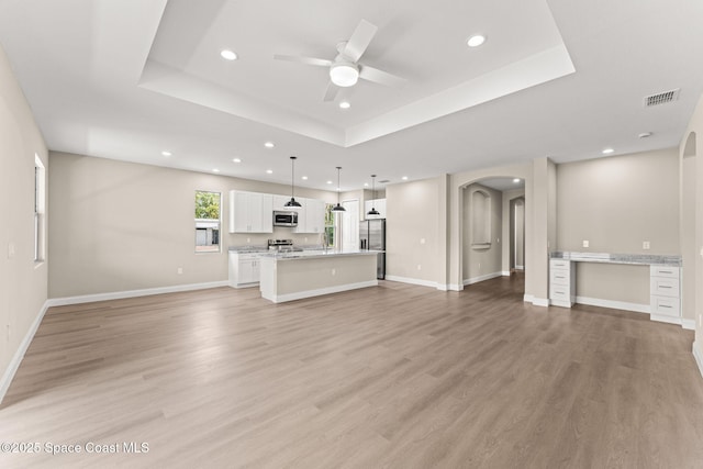 unfurnished living room featuring arched walkways, a raised ceiling, recessed lighting, ceiling fan, and light wood finished floors