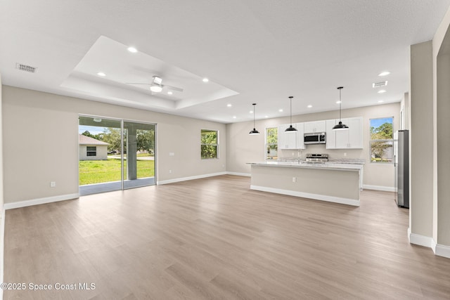 unfurnished living room with a ceiling fan, baseboards, light wood-style floors, recessed lighting, and a raised ceiling