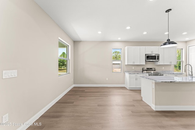 kitchen with stainless steel appliances, white cabinets, light stone counters, light wood finished floors, and recessed lighting