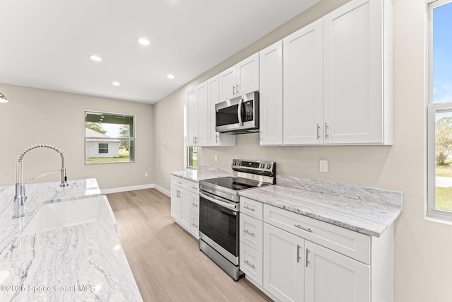 kitchen featuring stainless steel appliances, a sink, light wood finished floors, white cabinets, and recessed lighting