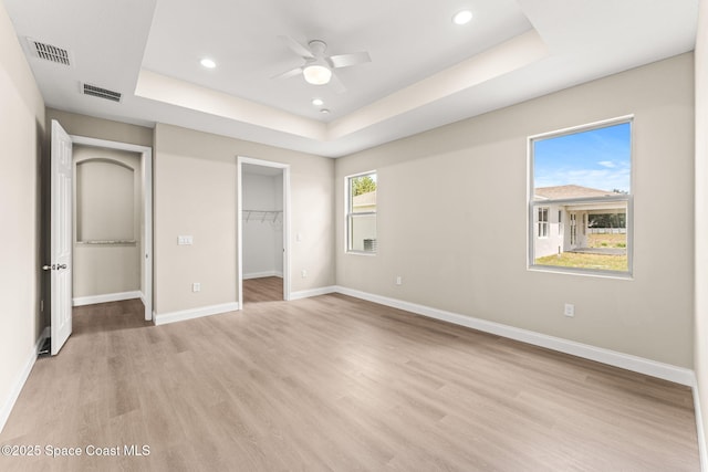 unfurnished bedroom with a raised ceiling, light wood-style flooring, baseboards, recessed lighting, and a walk in closet