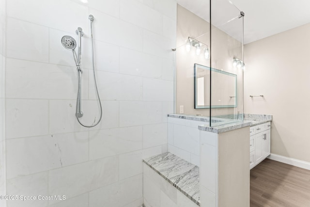 full bath with tiled shower, vanity, baseboards, and wood finished floors