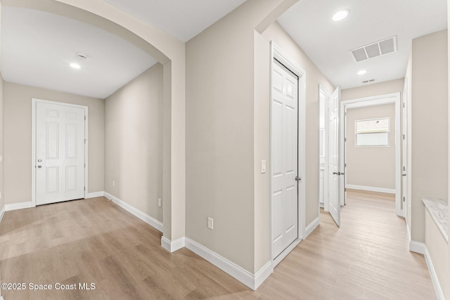 corridor featuring light wood-style flooring, arched walkways, baseboards, and recessed lighting