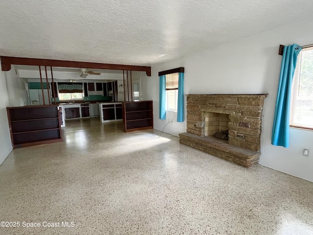 141 Valencia Rd, Rockledge, FL 32955 - unfurnished living room with a ceiling fan, speckle patterned floor, a textured ceiling, and a stone fireplace