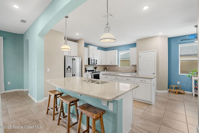 3575 Salt Marsh Cir, West Melbourne, FL 32904 - kitchen featuring stainless steel appliances, an island with sink, arched walkways, light tile patterned flooring, and backsplash