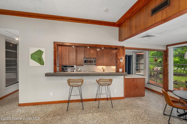 2318 Country Club Rd, Melbourne, FL 32901 - kitchen featuring stainless steel appliances, brown cabinetry, backsplash, ornamental molding, and light carpet