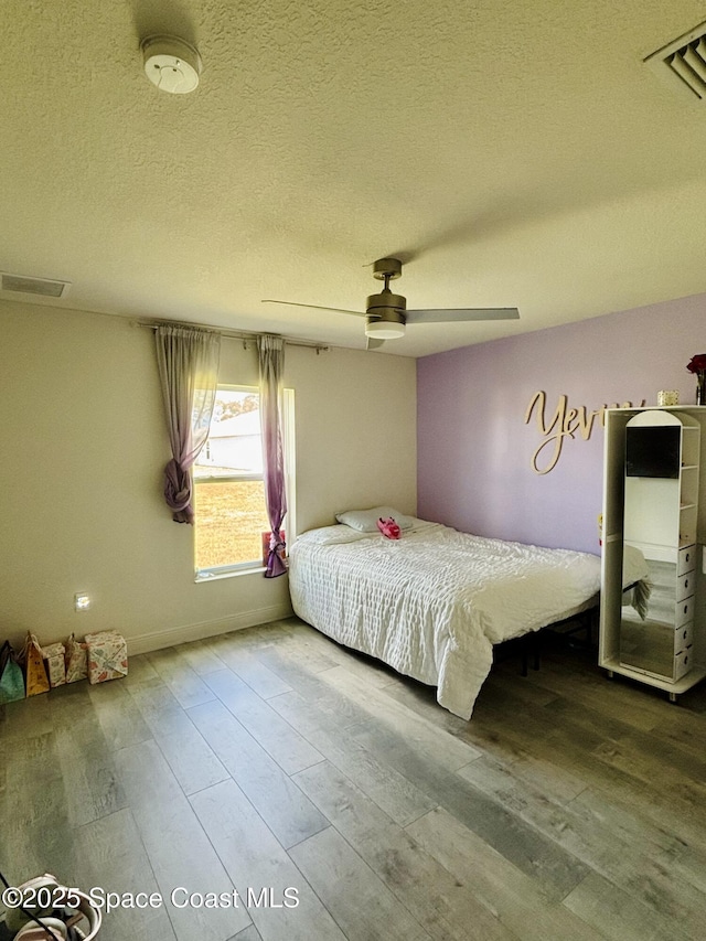 bedroom with wood finished floors, a textured ceiling, a ceiling fan, and baseboards