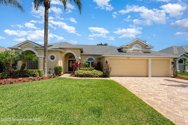 mediterranean / spanish home featuring stucco siding, an attached garage, a front lawn, and decorative driveway