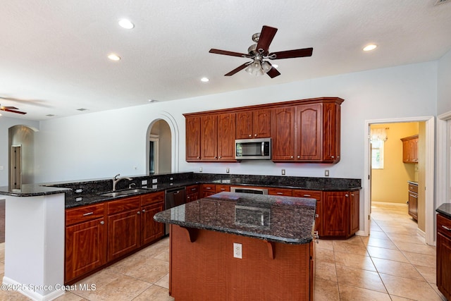 kitchen featuring appliances with stainless steel finishes, ceiling fan, a sink, arched walkways, and a peninsula