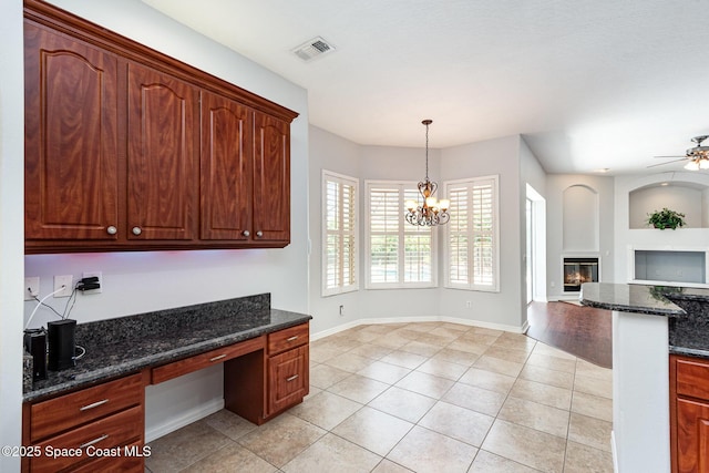 unfurnished office with built in study area, a glass covered fireplace, light tile patterned floors, ceiling fan, and baseboards