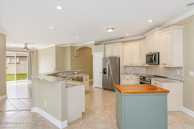 kitchen featuring appliances with stainless steel finishes, a large island with sink, butcher block counters, arched walkways, and ornamental molding