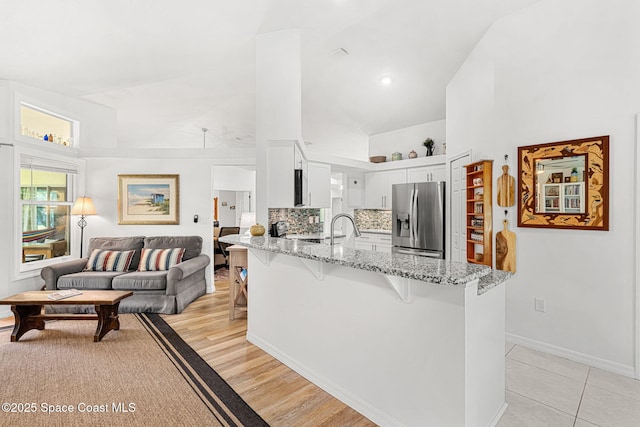 722 Hyannie St NE, Palm Bay, FL 32907 - kitchen with stainless steel fridge with ice dispenser, a peninsula, a breakfast bar area, a towering ceiling, and white cabinetry
