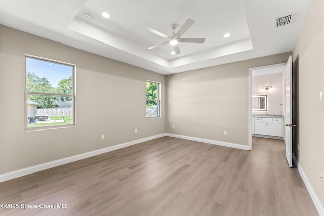 563 Holmes Ave NW, Palm Bay, FL 32907 - unfurnished bedroom featuring a raised ceiling, light wood-style floors, recessed lighting, baseboards, and ensuite bath