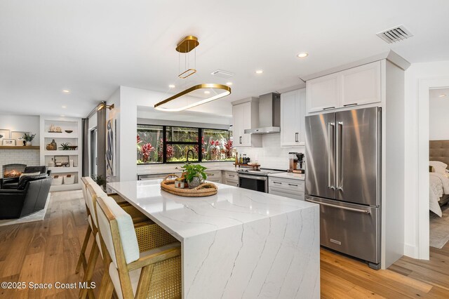 3204 Nottingham Ln, Cocoa, FL 32926 - kitchen featuring appliances with stainless steel finishes, wall chimney range hood, light stone countertops, light wood finished floors, and backsplash