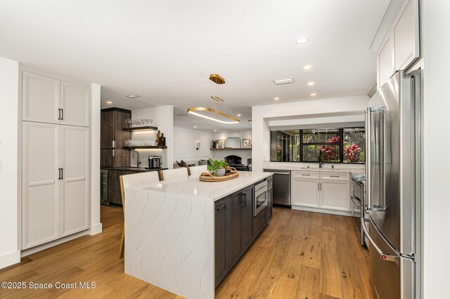 3204 Nottingham Ln, Cocoa, FL 32926 - kitchen with stainless steel appliances, white cabinetry, light wood-style flooring, light stone counters, and a kitchen island