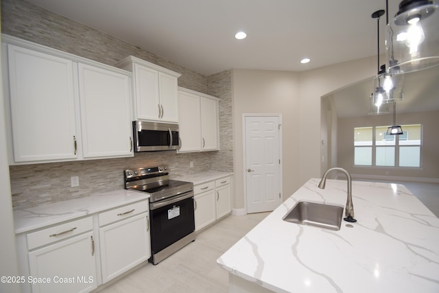 kitchen featuring stainless steel appliances, a sink, arched walkways, decorative backsplash, and white cabinets