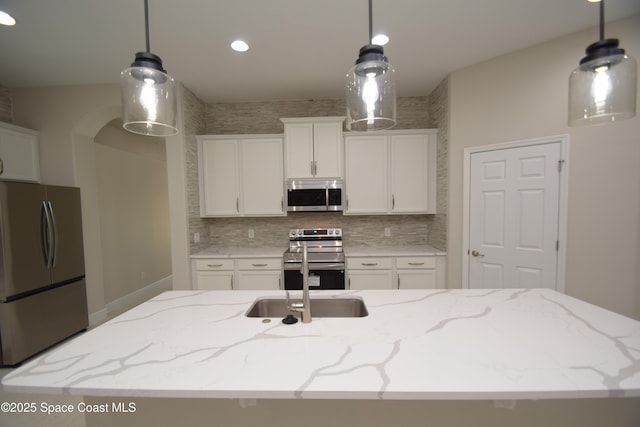 kitchen featuring appliances with stainless steel finishes, white cabinetry, decorative backsplash, light stone countertops, and decorative light fixtures