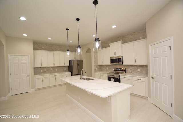 kitchen with stainless steel appliances, arched walkways, tasteful backsplash, a center island with sink, and a sink