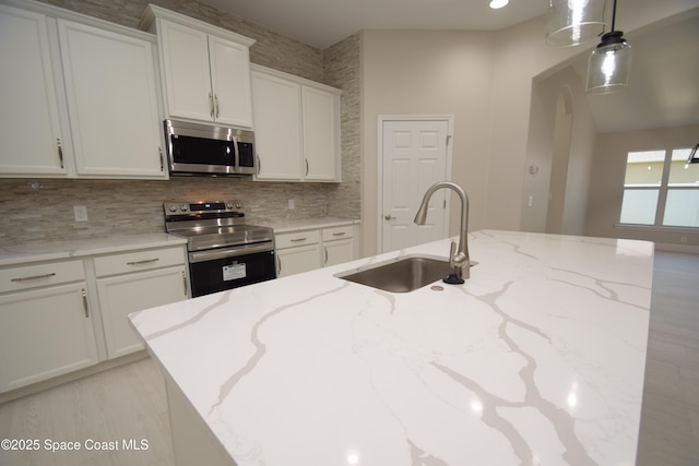 kitchen with stainless steel appliances, a sink, backsplash, white cabinetry, and light stone countertops