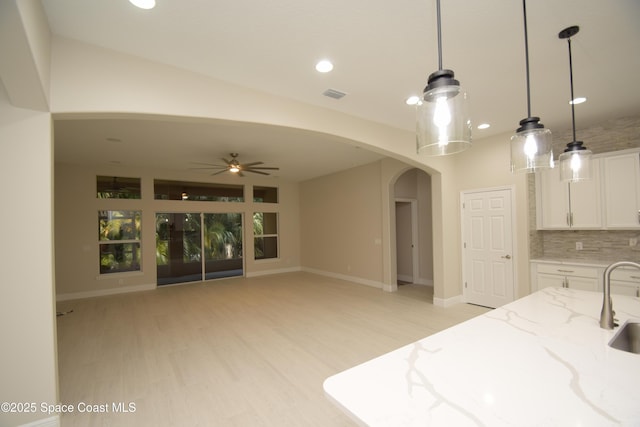 kitchen featuring arched walkways, white cabinets, ceiling fan, light stone counters, and decorative backsplash