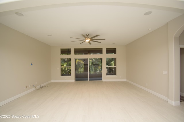 empty room featuring light wood finished floors, ceiling fan, arched walkways, and baseboards
