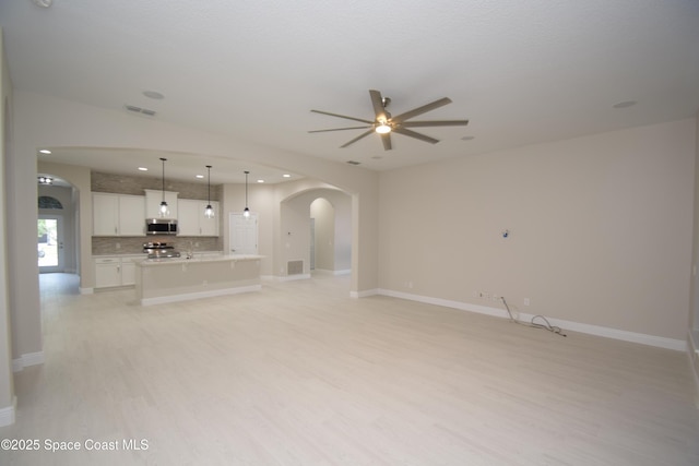 unfurnished living room featuring arched walkways, a ceiling fan, light wood-style floors, baseboards, and recessed lighting