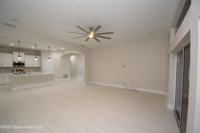 unfurnished living room featuring arched walkways, ceiling fan, light wood-type flooring, recessed lighting, and a sink