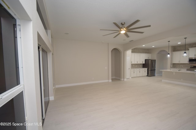 unfurnished living room featuring arched walkways, ceiling fan, light wood finished floors, baseboards, and recessed lighting