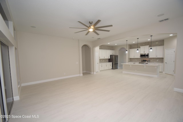unfurnished living room featuring arched walkways, ceiling fan, recessed lighting, light wood-type flooring, and baseboards