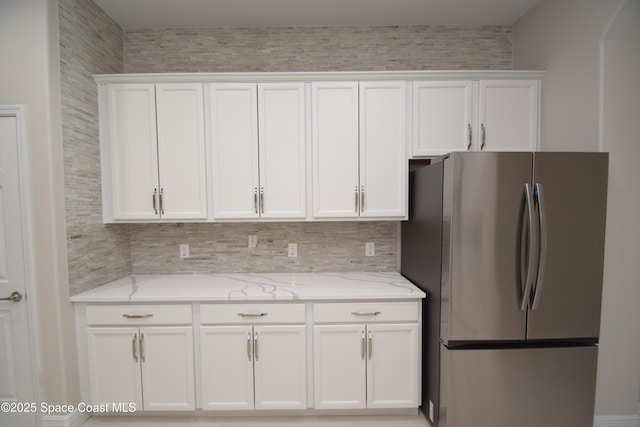 kitchen with freestanding refrigerator, white cabinetry, light stone counters, and tasteful backsplash