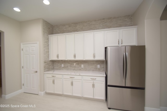 kitchen featuring freestanding refrigerator, white cabinets, baseboards, light stone countertops, and recessed lighting