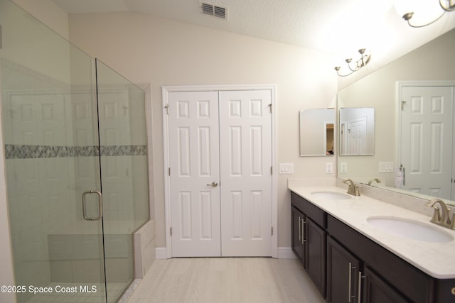 bathroom with lofted ceiling, a shower stall, wood finished floors, double vanity, and baseboards