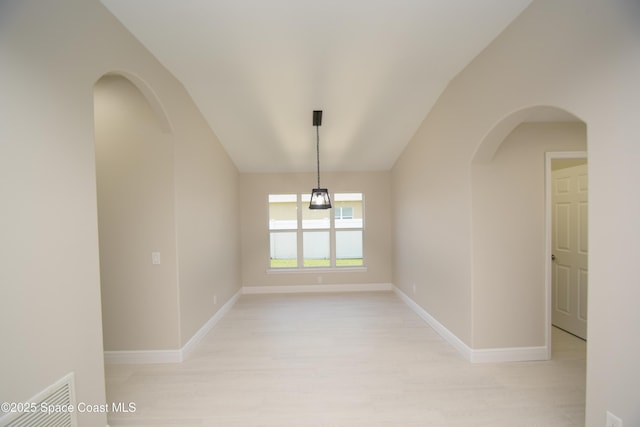 spare room featuring light wood-type flooring, baseboards, vaulted ceiling, and arched walkways