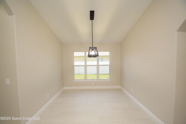 unfurnished room featuring light wood-style flooring, lofted ceiling, baseboards, and arched walkways