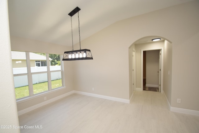 empty room with vaulted ceiling, arched walkways, light wood-style flooring, and baseboards