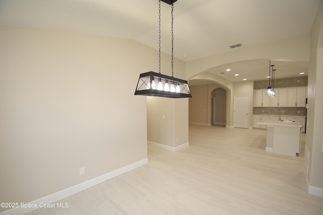 detailed view of arched walkways, a sink, recessed lighting, decorative backsplash, and wood finished floors