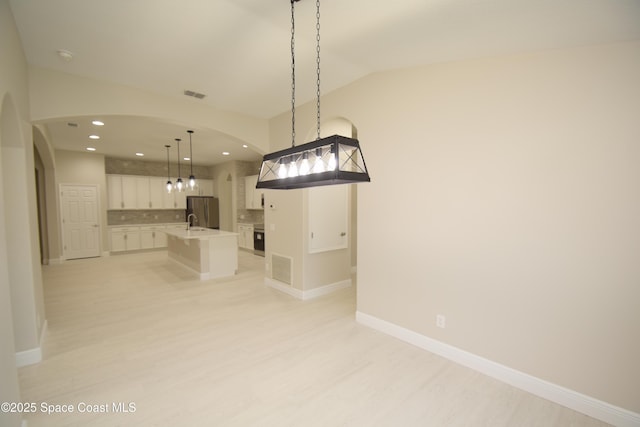 kitchen featuring freestanding refrigerator, white cabinets, light wood finished floors, tasteful backsplash, and an island with sink