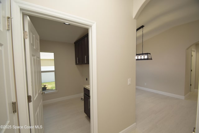 hall with arched walkways, light wood finished floors, baseboards, and vaulted ceiling
