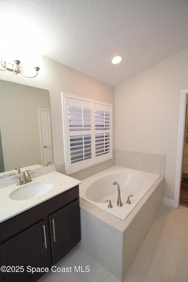full bath with a textured ceiling, a bath, vanity, and recessed lighting