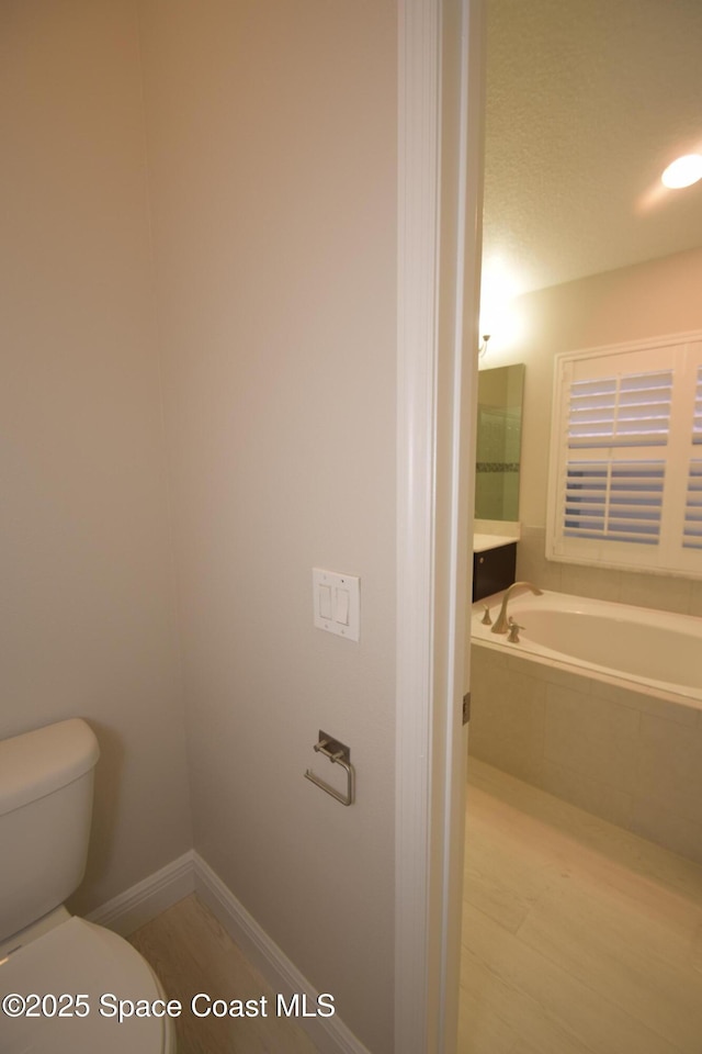 bathroom with toilet, wood finished floors, and a bath