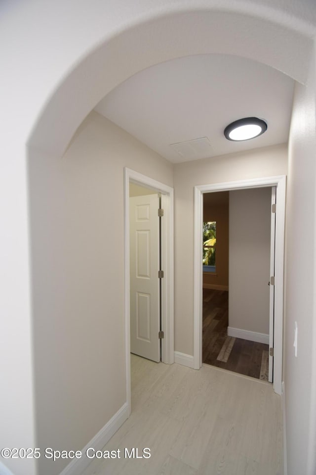 corridor featuring wood finished floors, arched walkways, and baseboards