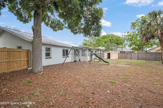 fenced backyard with a playground, a storage unit, and an outdoor structure