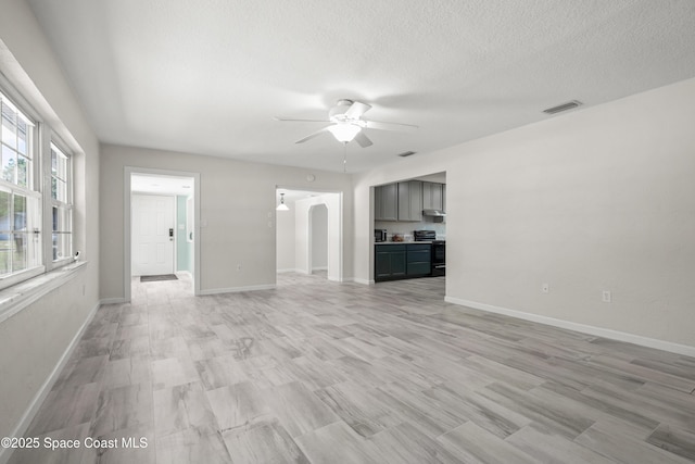 unfurnished living room featuring a ceiling fan, arched walkways, light wood-style floors, a textured ceiling, and baseboards